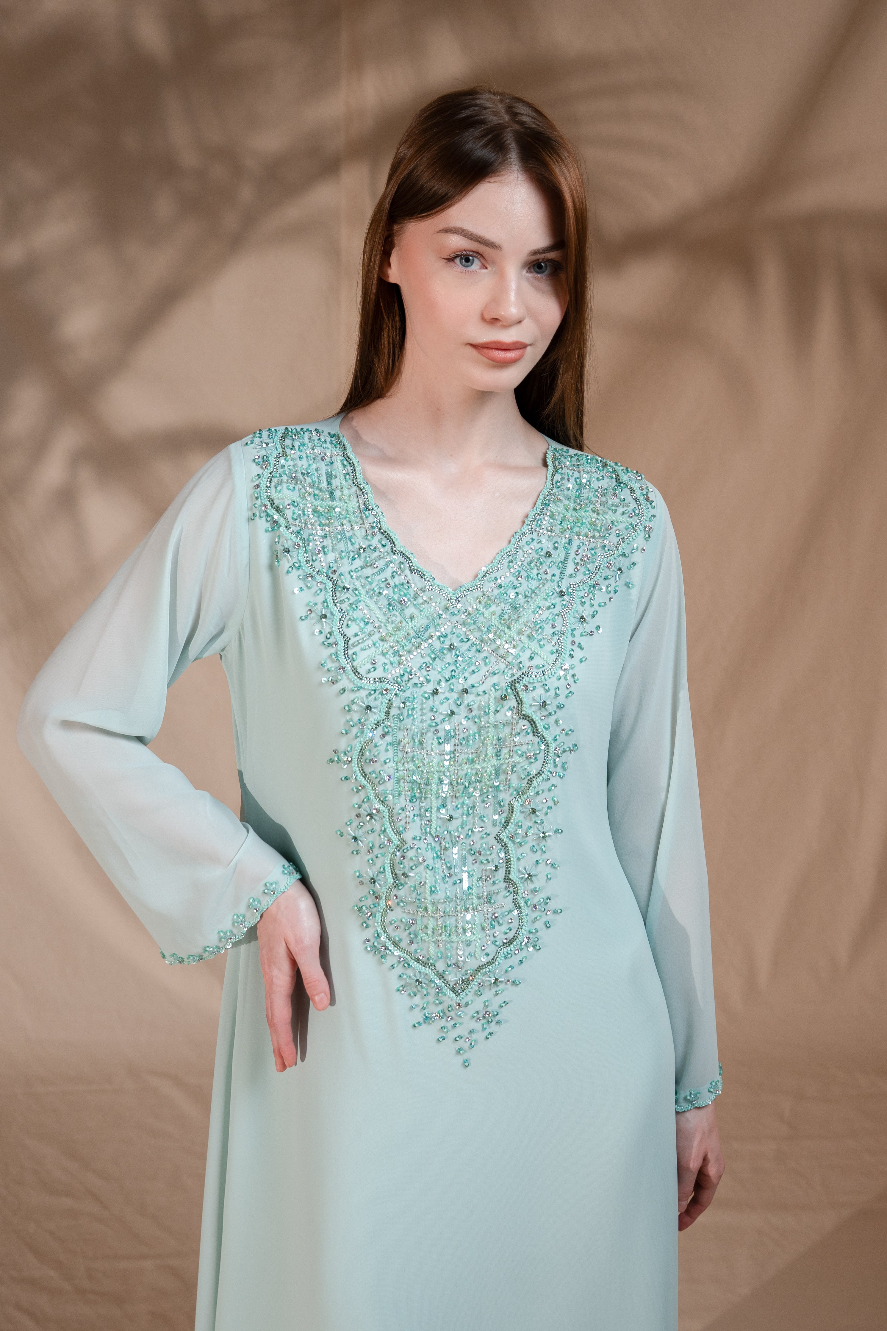 Woman wearing a light blue dress with intricate beadwork against a beige background